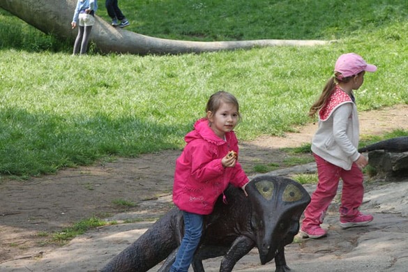 Weronika z pączkiem siedzi na kamiennym dinozaurze – radość.