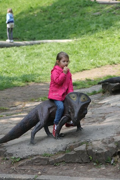 Weronika siedzi na kamiennym dinozaurze – kolejne ujęcie.