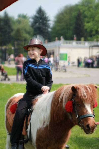 Mały kowboj Maciej uśmiecha się na kucyku w zoo.